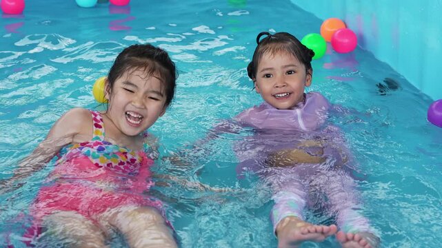 slow motion of happy preschool child girl playing together with her sister in outdoor portable swimming pool in backyard at home