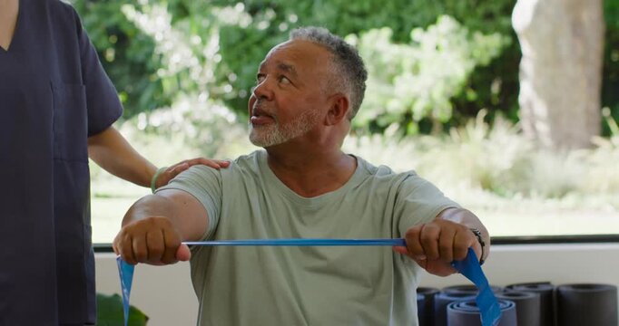 African-American senior seated pulling blue resistance band following therapist cues in clinic