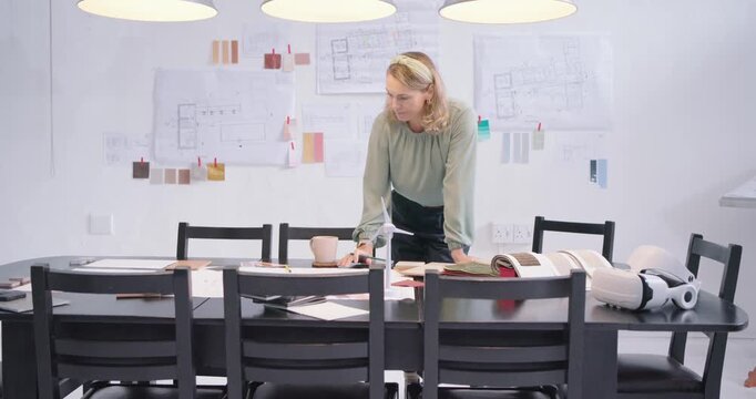 Woman wearing green blouse approaching dark table in studio, reviewing swatches, marking final plan