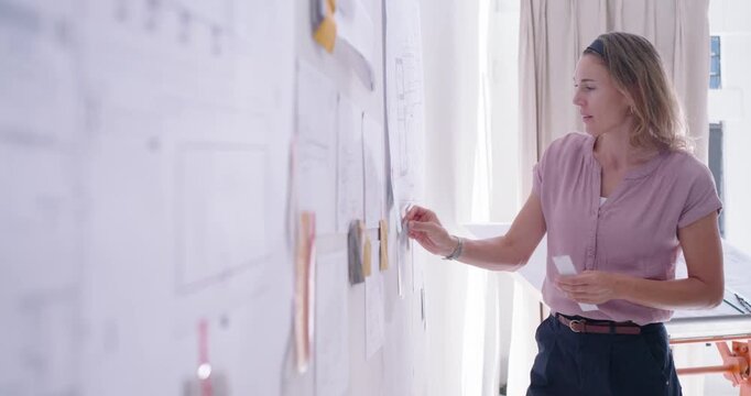 Mid-adult woman after board review, wearing pink blouse in studio, moving sticky notes, copy space
