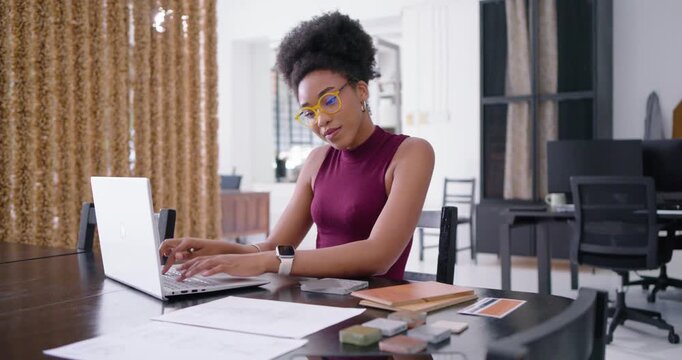 Woman checking laptop, typing and marking sample swatches at bright home studio preparing pitch