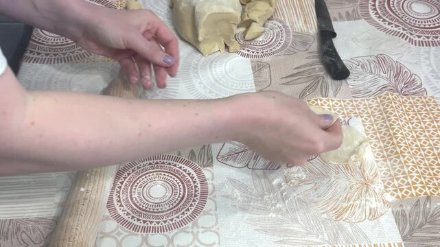 Close up of a woman shaping and rolling thin dough circles for dumplings on a kitchen table, culinary task, domestic lifestyle, food preparation.