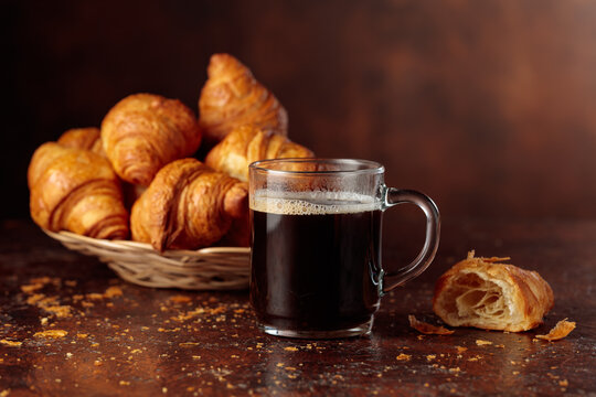 Black coffee and croissants on a brown background.