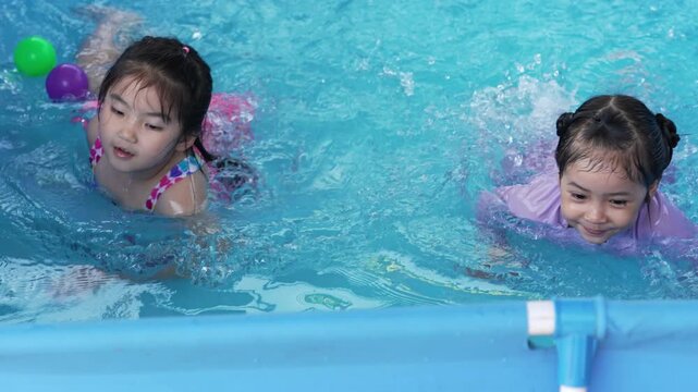 slow motion of happy preschool child girl playing together with her sister in outdoor portable swimming pool in backyard at home