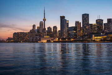Naklejka premium Illuminated Toronto city skyline at sunset on Lake Ontario - Toronto, Ontario, Canada