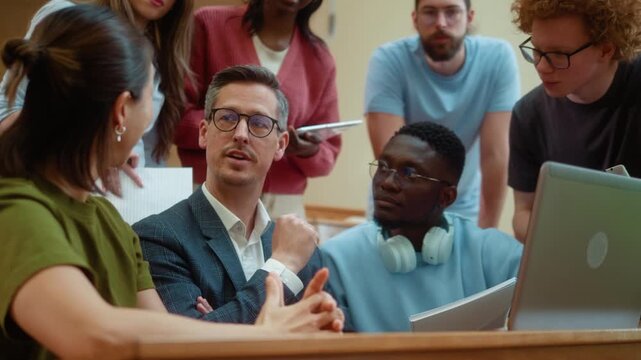 Male professor listening carefully to students during collaborative laptop session at university. Friendly teamwork atmosphere ending with genuine laughter and positive communication.