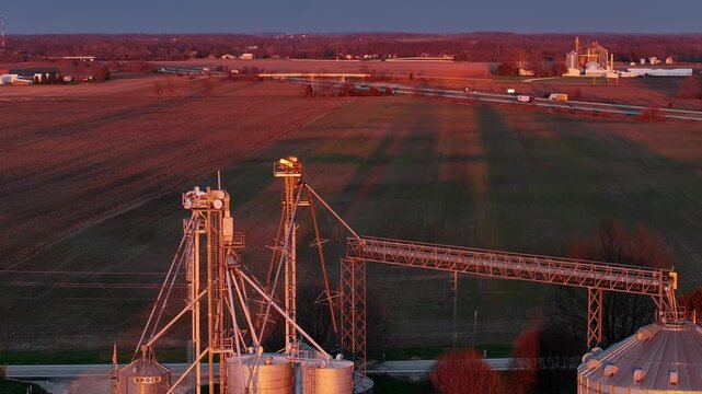 Aerial view of industrial grain elevators and agricultural structures overlooking vast fields and a distant highway during golden hour in Wilmington, Ohio, United States.