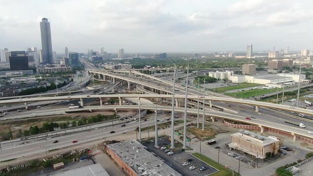 Aerial view of a complex highway interchange and the city skyline under a cloudy sky in Houston, Texas, United States.