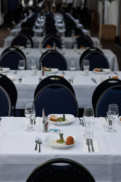 Elegant restaurant table setting with white linen, plates, cutlery and wine glasses in bright natural sunlight. Indoor fine dining scene, showcasing luxury hospitality atmosphere