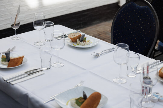 Elegant restaurant table setting with white linen, plates, cutlery and wine glasses in bright natural sunlight. Indoor fine dining scene showcasing luxury hospitality atmosphere