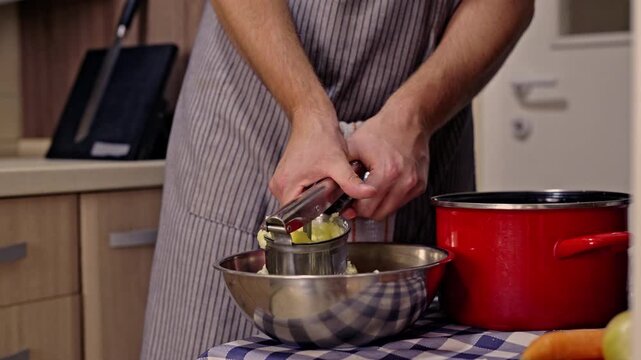 A person is preparing mashed potatoes in a home kitchen. The chef uses a potato ricer to mash boiled potatoes into a bowl for a fresh, healthy, and delicious homemade meal.