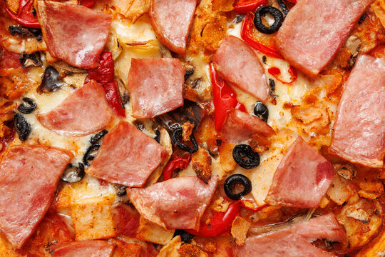 Close up of homemade pizza with ham mushrooms olives and sweet pepper melted cheese texture hot fresh comfort food