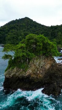 Aerial view of the rocky islet of Bahia Solano with lush vegetation and turquoise waves crashing against the cliffs in Mutis, Choco, Colombia.
