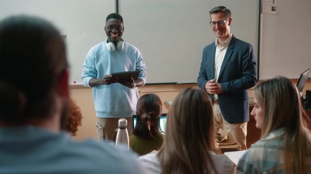 African male student presenting project with tablet beside professor during university class. Academic presentation, thesis discussion and collaborative learning.