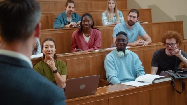 Group of smiling diverse students raising hands in university amphitheater after teacher asked question during lecture.