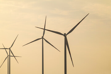 Fototapeta premium Wind turbines stand tall against a hazy sunset sky in a renewable energy field