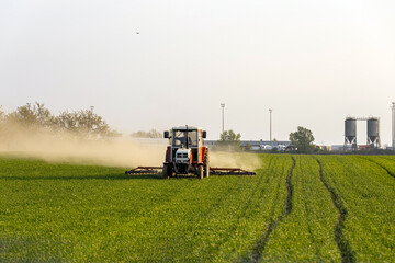 Fototapeta premium Tractor working in field under clear sky during late afternoon in farming area