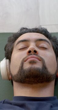 Vertical video: African man lying on green mat, headphones playing, meditating with hands in prayer