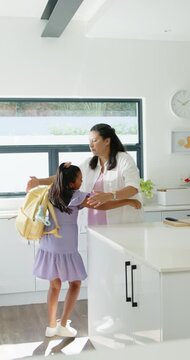 Vertical video: Mother and child placing yellow backpack in kitchen hugging leaving for school