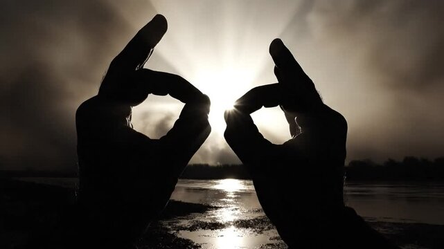 Silhouetted hands creating an ok symbol shape around the sun on a cloudy morning