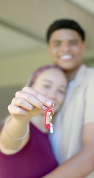 Vertical video: Diverse couple holding red key fob on porch after getting keys, celebrating home