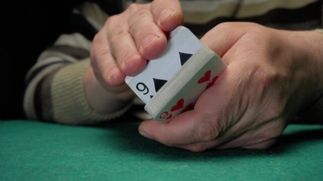 Hands of a person shuffling playing cards on a green felt table, showcasing the action of mixing cards in a casual indoor setting