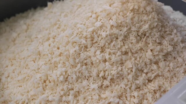 A close-up, slow-motion shot of golden-white panko breadcrumbs cascading down to form a large, textured pile, highlighting the light and airy flakes used for crispy breading and culinary applications.