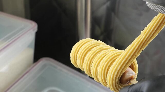 Close-up shot of a hand in a black glove wrapping a cheese stick on a small wooden skewer with extruded churro dough. This popular street food snack combines the savory taste of mozzarella cheese with