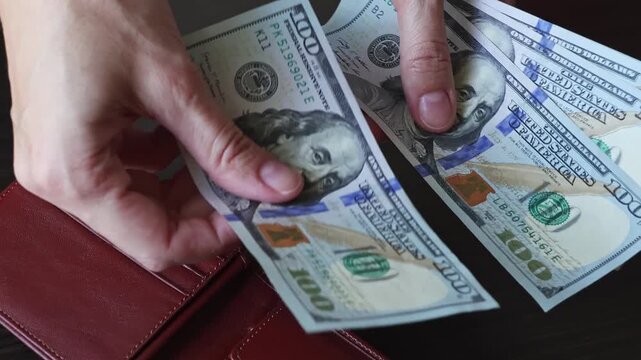 Female hands count 100 american dollar notes (USD) and put them in a leather wallet. Concept of money savings, financial income, making profits and dividends. Close-up real time footage.