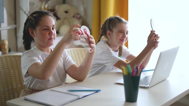 Two girl students learn online with number cards laptop at home. Sisters study together during remote education. Girls practice math with flashcards. Students learning at desk with notebook laptop.