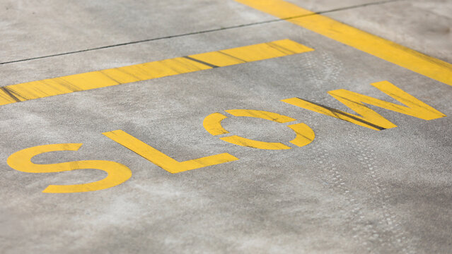 Yellow slow road marking painted on gray asphalt surface, indicating traffic safety, caution, and regulating vehicle speed in a designated zone