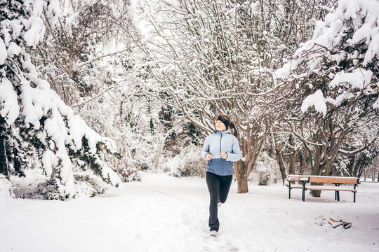Young woman jogging in a snowy park surrounded by trees covered in fresh snow