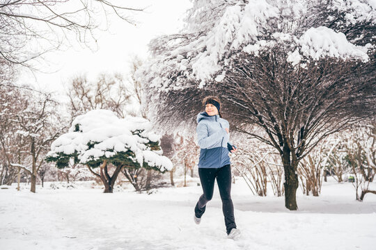 Female runner training outdoors in winter, surrounded by snow-covered trees