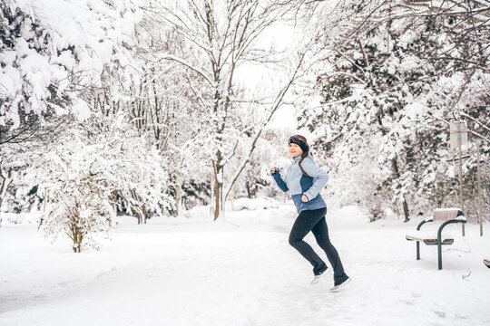 Woman jogging through snowy park, maintaining fitness during winter season
