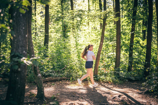 Athletic woman jogging through lush green forest, enjoying peaceful nature and fitness routine
