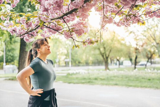 Young woman standing under cherry blossom tree, enjoying spring moment after workout