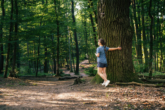 Young woman taking a break, stretching and leaning on a tree during outdoor training in the forest