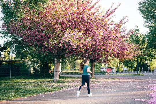 Woman jogging under vibrant cherry blossom trees, enjoying spring fitness routine