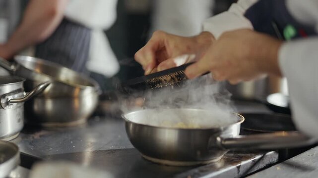 Steam rises from a steaming pan. Chef's hands sprinkle seasoning with precision. Focus is on the cooking process. Professional kitchen environment. Dramatic close-up of culinary action