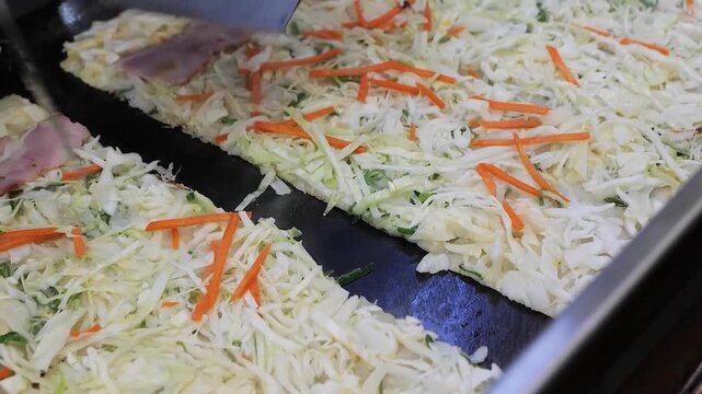 A close-up, high-angle view of a large batch of freshly prepared coleslaw or cabbage and carrot salad in a metal serving tray. The salad consists of finely shredded white cabbage and julienned orange 