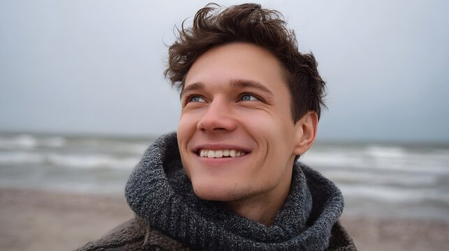 A young man smiles while standing on a serene beach gazing out towards the vast open ocean under an overcast sky