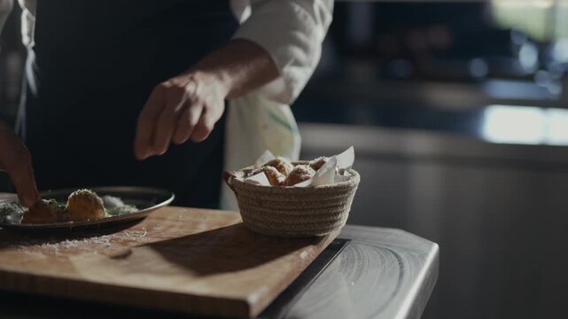 Hands craft bread rolls with care and precision. Warm bread rests in a woven basket beside a wooden board. Chef's focused movements convey culinary dedication. Perfect for food, cooking
