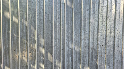 Fototapeta premium A close-up view of a vertical corrugated galvanized steel fence, showing metallic textures and dappled shadows from nearby foliage.