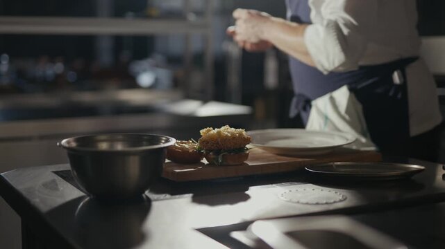 Chef prepares a dish with care and precision. Hands move gently over ingredients, showing focus and skill. Plates appear ready, suggesting a fine dining setting