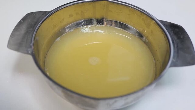 A detailed shot of a person wearing blue nitrile gloves operating a manual stainless steel citrus press. The footage shows the process of extracting fresh, tart lemon juice, which collects in the meta