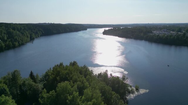 Aerial drone footage of the scenic Kaukaj&auml;rvi beach area in Kangasala, Finland during a bright summer day. The image shows a calm lakeside landscape surrounded by green forest, sandy beach, and clear 