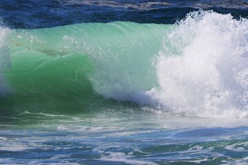 Obraz premium Sunny warm day on a Portuguese beach with people sunbathing and swimming in the ocean. Big waves attract surfers riding the Atlantic, creating a lively summer seaside atmosphere.