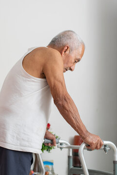 Elderly man using walker for mobility support while moving carefully inside his home