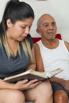 Close up of young woman reading book while elderly grandfather listens attentively beside her