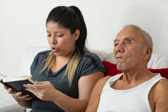 Young woman guiding elderly grandfather through reading activity with patience and care